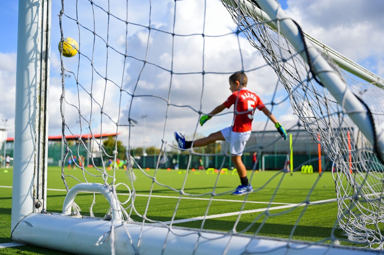 A young player shooting towards goal, seen through the net