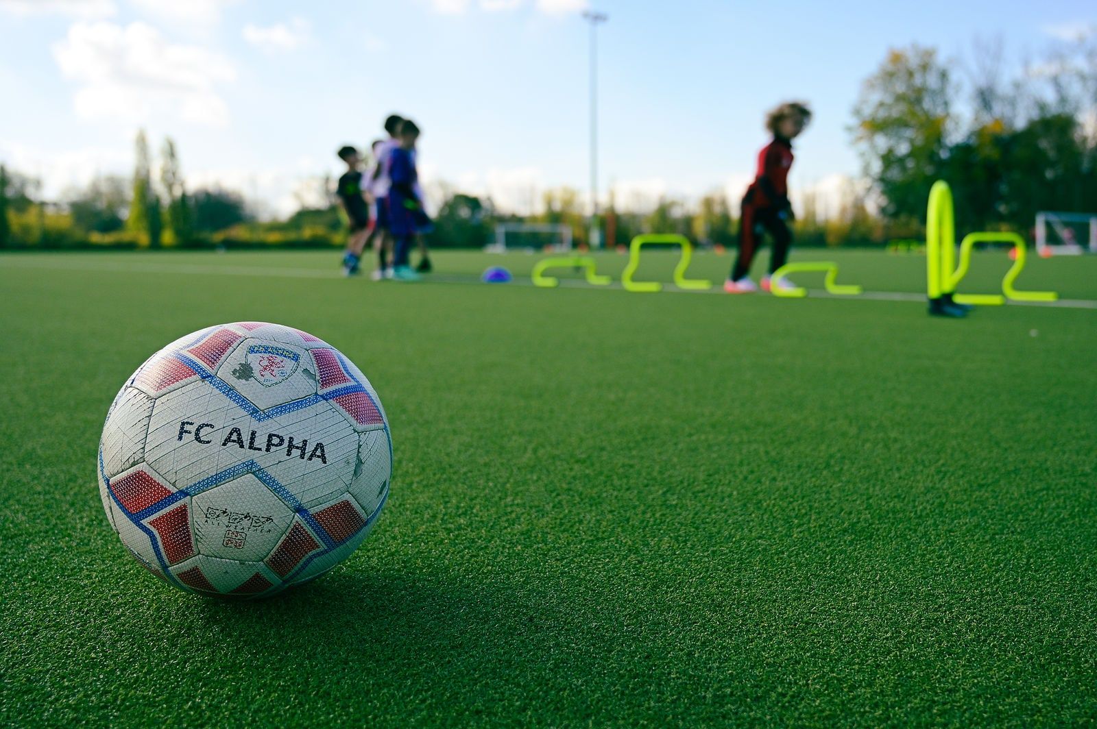 An FC Alpha ball on the pitch with a training session behind it