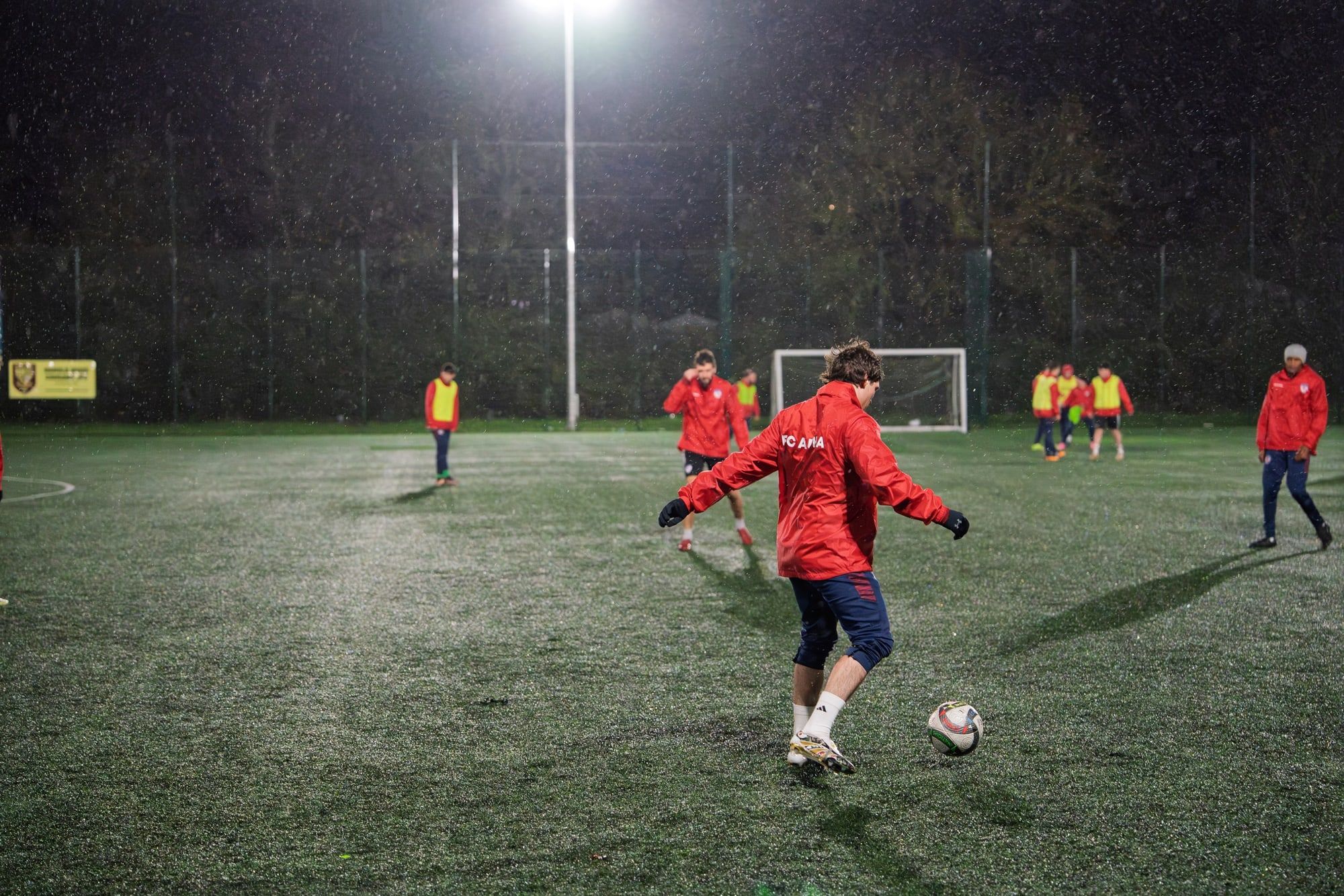 A senior player striking the ball with team-mates training behind